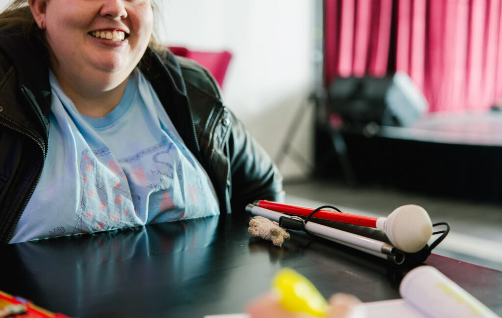 A woman is sitting talking to someone unseen across a table. she has a cane folded up on the table in front of her.